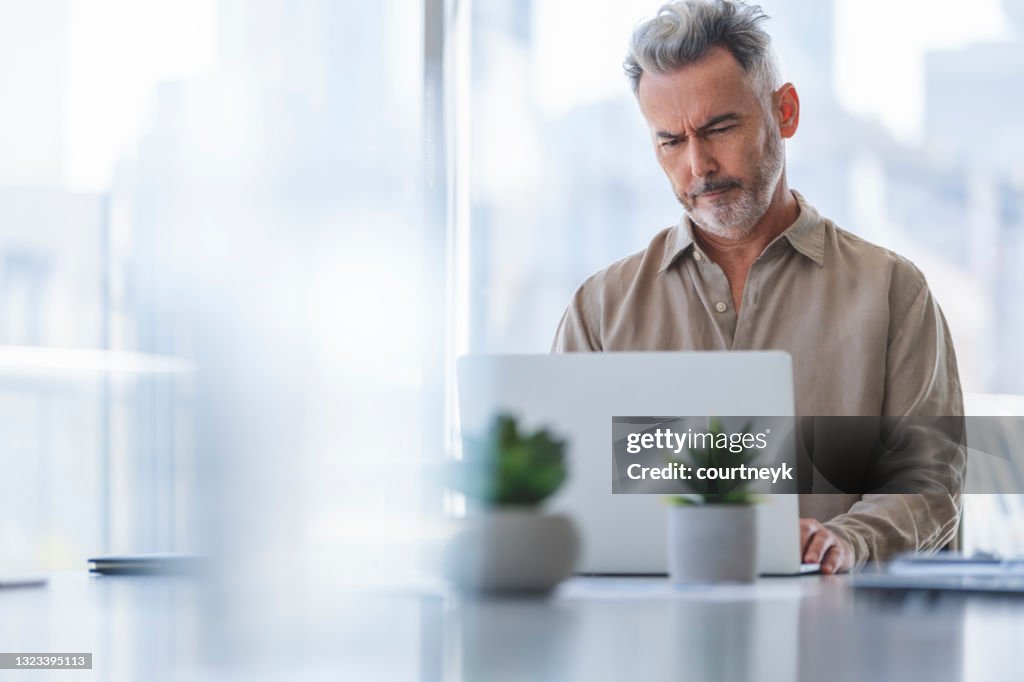 Reifer Geschäftsmann, der an einem Schreibtisch auf einem Laptop arbeitet.