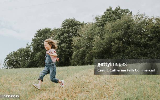 little girl runs fast across a vast grassy area, while laughing - bambini che corrono foto e immagini stock