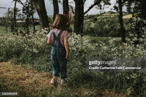 young girl stands outside, admiring nature, surrounded by cow parsley, trees, and wildflower. - cow parsley stockfoto's en -beelden