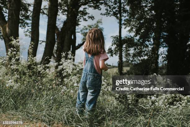 young girl stands outside, admiring nature, surrounded by cow parsley, trees, and wildflower. - cow parsley stockfoto's en -beelden