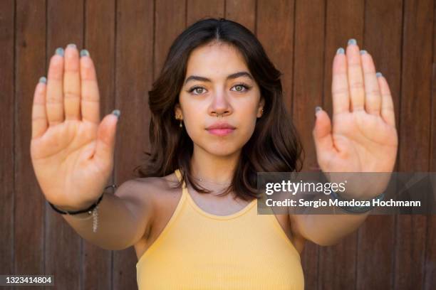 young latino woman looking at the camera and gesturing to stop with both hands, brown wooden background - femicide stock pictures, royalty-free photos & images