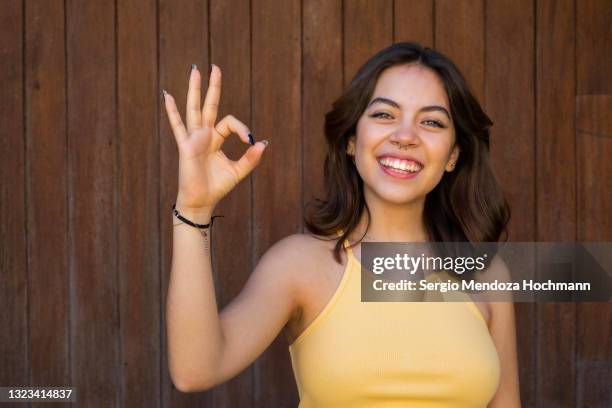 young latino woman looking at the camera and giving the ok sign, brown wooden background - gesturing ok stock pictures, royalty-free photos & images