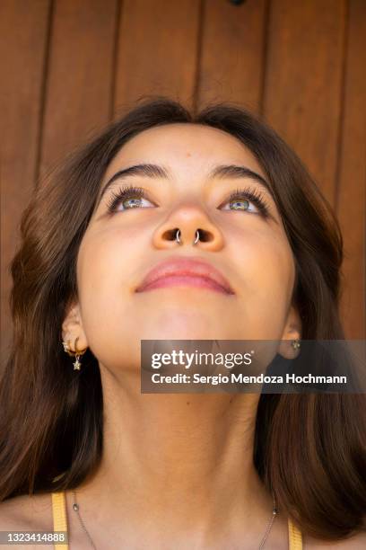 young latino woman looking up and showing a nose ring piercing, brown wooden background - septum stock pictures, royalty-free photos & images