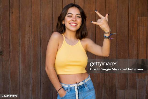 latino woman smiling, looking at the camera and doing the heavy metal horns hand sign, brown wooden background - anti bullying stockfoto's en -beelden