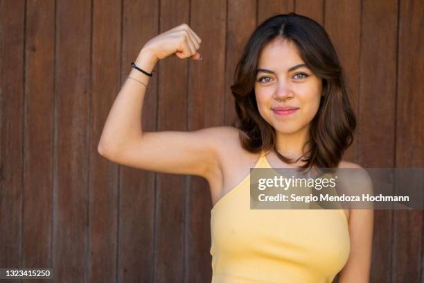 latino woman flexing her muscles and showing strength and determination, brown wooden background - mujeres mexicanas fotografías e imágenes de stock