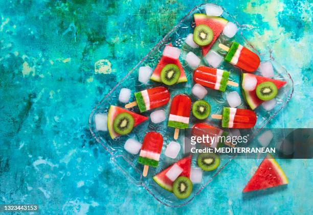 watermelon and kiwi popsicles in a watermelon slices and kiwi fruits with ice cubes glass tray over green - ice lolly stock pictures, royalty-free photos & images