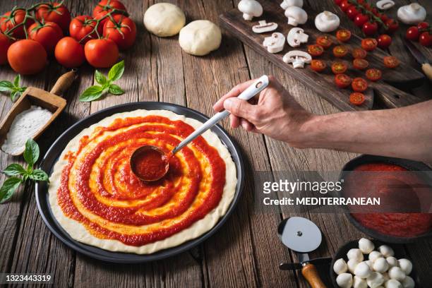 italiaanse pizza mannelijke hand pollepel die tomatensaus op pizzadeeg met ingrediëntenmozzarella spreidt - tomatensaus stockfoto's en -beelden