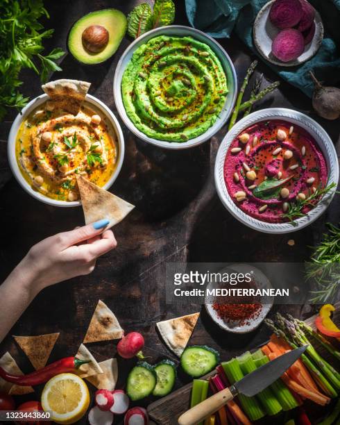 hummus bowls of chickpeas, avocado and beetroot female hand dip with cut vegetables for dipping - lebanese stock pictures, royalty-free photos & images