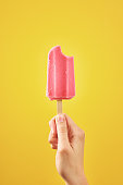 Bitten red frozen fruit ice cream popsicle on yellow background