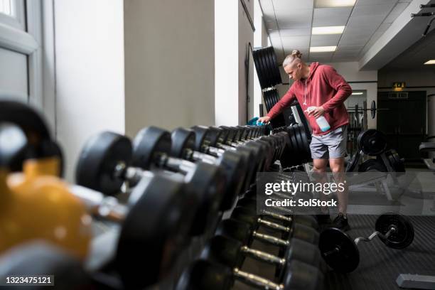 young man disinfecting weights in the gym - gym covid stock pictures, royalty-free photos & images