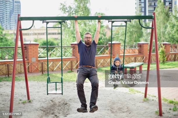 young father and his little son on a swing - playground stock-fotos und bilder