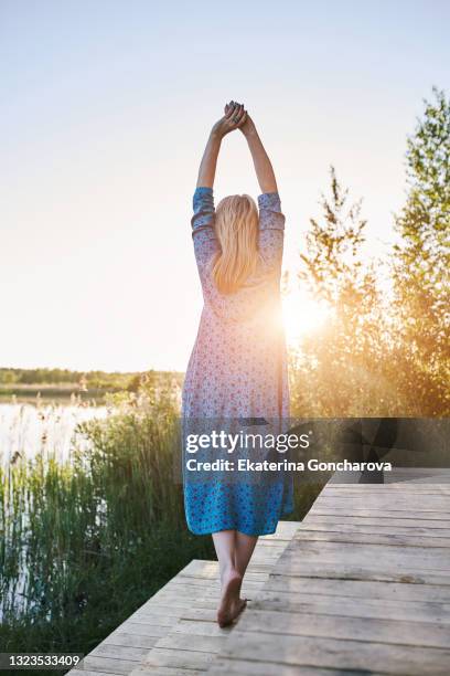 a beautiful 45-year-old woman in a blue dress spread her arms out to the sides in nature. - spread joy stock pictures, royalty-free photos & images