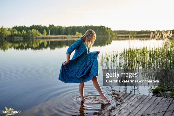 a 45-year-old woman in a blue dress walks on the water in nature. rest and relaxation in summer - women in see through dresses stock-fotos und bilder