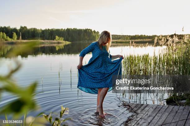 a 45-year-old woman in a blue dress walks on the water in nature. rest and relaxation in summer - 45 49 år bildbanksfoton och bilder