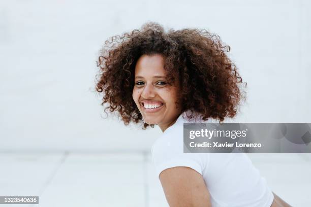 portrait of young woman with afro hair smiling at camera - afro frisur stock-fotos und bilder