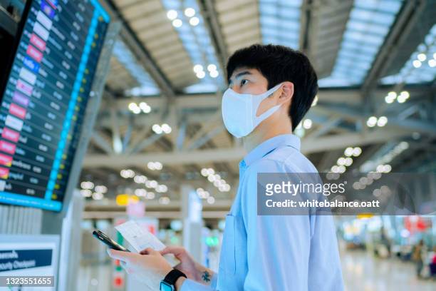 ung asiatisk man kontrollerar avgångsbräda med smart telefon på flygplatsen - dykmask bildbanksfoton och bilder