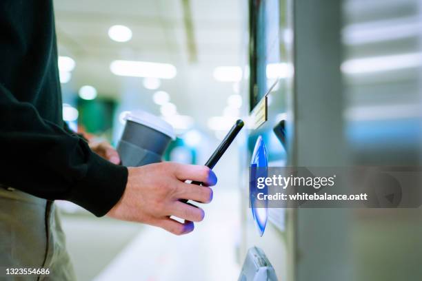 nahaufnahme eines jungen asiatischen mannes mit kontaktlosem bezahlen per smartphone, um ihren einkauf am self-checkout-kiosk in der u-bahn zu bezahlen - application modernization stock-fotos und bilder