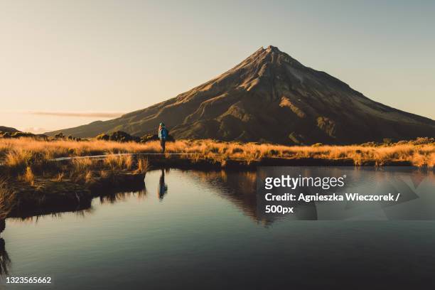 man standing by lake against clear sky during sunset,taranaki,new zealand - new zealand volcano stock pictures, royalty-free photos & images