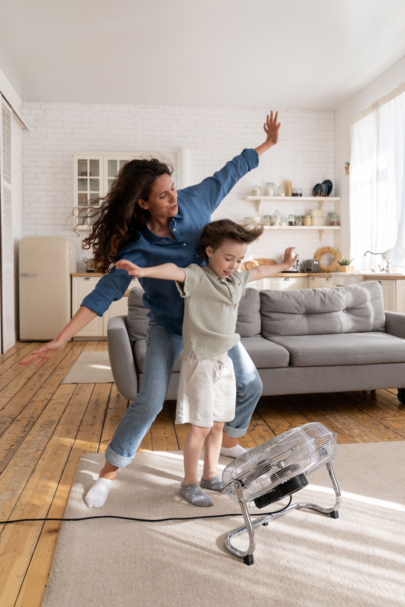 Overjoyed mom and small kid have fun at home play with wind from ventilator cheering and bonding Overjoyed mom and small kid have fun at home play with wind from ventilator cheering and bonding
