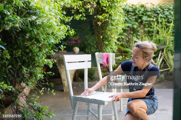 diy: woman sanding wooden chairs in back yard - garden furniture stockfoto's en -beelden