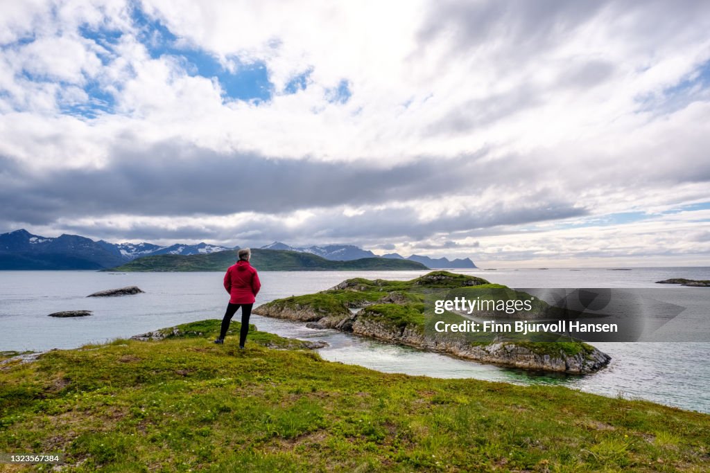 Senior woman standing on a mountain covered in grass - looking out over the ocean