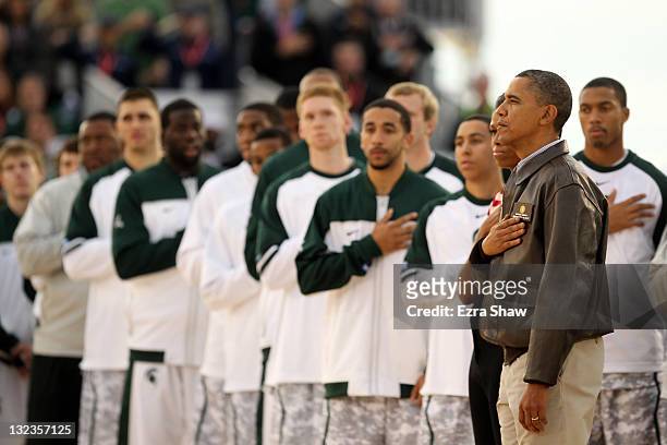 President Barack Obama and first lady Michelle Obama stand next to the Michigan State Spartans during the United States National Anthem before the...