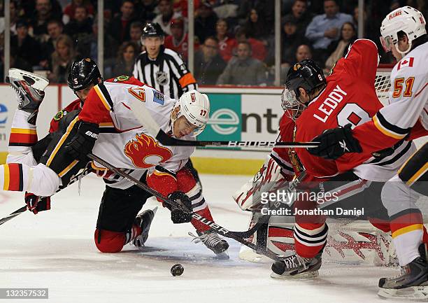 Rene Bourque of the Calgary Flames falls trying to shoot the puck against Ray Emery and Nick Leddy of the Chicago Blackhawks at the United Center on...