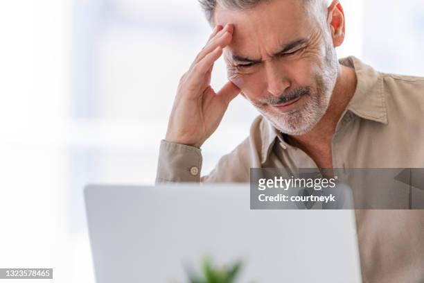 hombre de negocios maduro que trabaja en un escritorio en una computadora portátil. - entrecerrar los ojos fotografías e imágenes de stock
