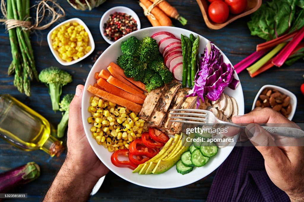 Gesunde Ernährungs- und Ernährungskonzepte. Top-Ansicht der Menschen Hände halten einen gesunden frischen Salat in einer Schüssel mit rohem Gemüse im Hintergrund.