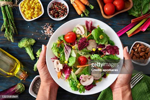 gesunde ernährungs- und ernährungskonzepte. top-ansicht der frauen hände halten einen gesunden frischen vegetarischen salat in einer schüssel mit rohem gemüse im hintergrund. - kopfsalat stock-fotos und bilder
