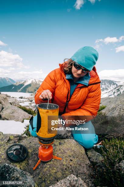 a female backcountry hiker crouches beside a camp stove on a alpine ridge - wilderness survival stock pictures, royalty-free photos & images