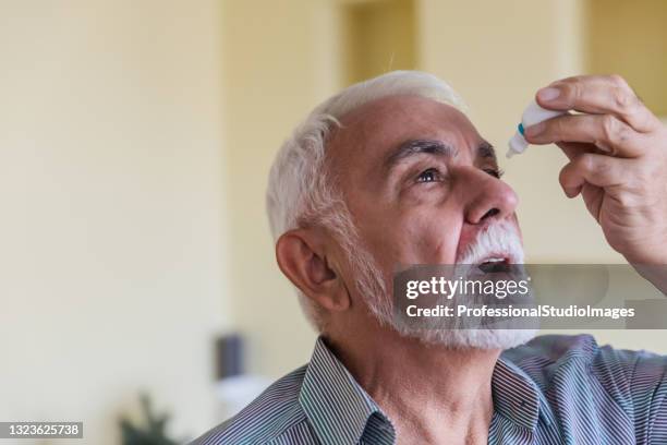 an older man is using eye drops for better vision. - eyedropper stock pictures, royalty-free photos & images