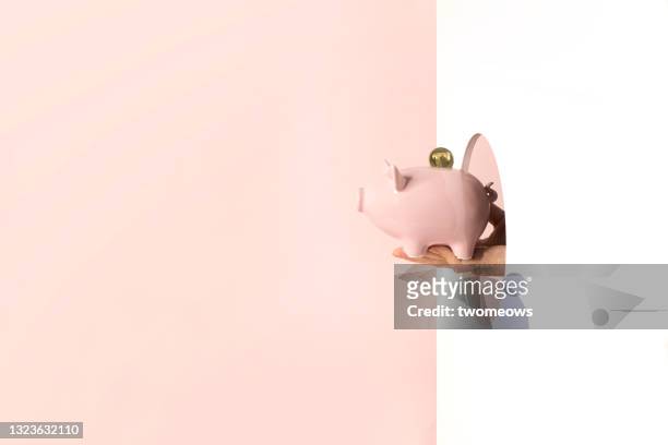 one hand holding piggy bank through an opening on wall. - passing giving stock pictures, royalty-free photos & images
