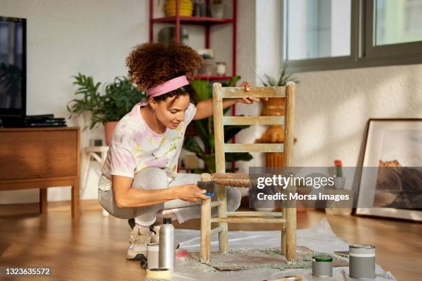 young woman scraping wooden chair in living room - do it yourself stock-fotos und bilder