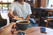 a man and a woman clinking coffee mugs in cafe