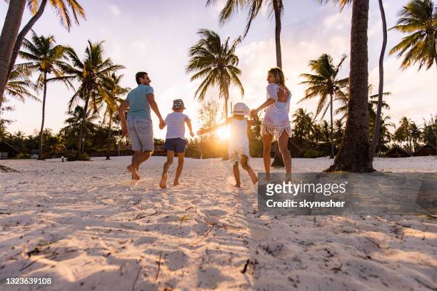 rückansicht der unbeschwerten familie, die bei sonnenuntergang am strand läuft. - beach holiday stock-fotos und bilder