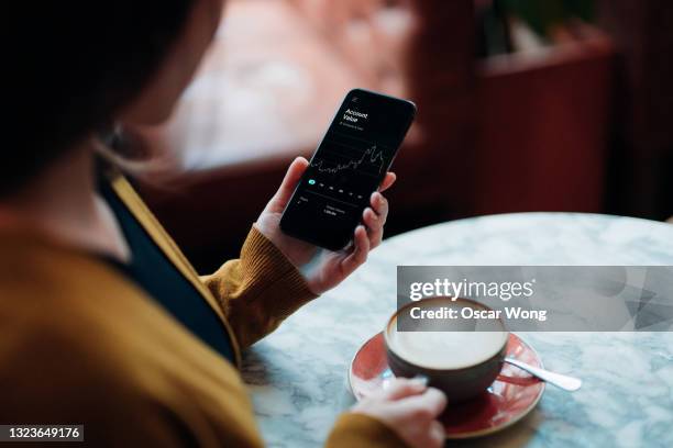 over the shoulder view of young woman checking financial trading data on smartphone in cafe - england media access fotografías e imágenes de stock