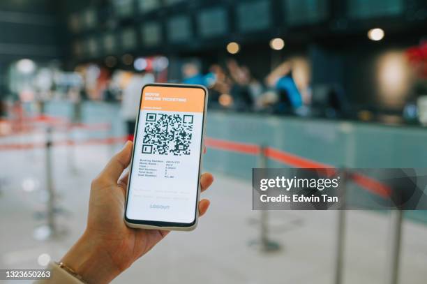 asian chinese woman using mobile app cinema movie e-ticketing reservation in front of cinema ticketing counter - hand paying smartphone stock pictures, royalty-free photos & images