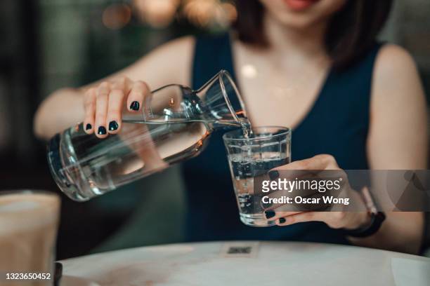 cropped shot of young woman pouring water to a drinking glass at cafe - sprudelgetränk stock-fotos und bilder