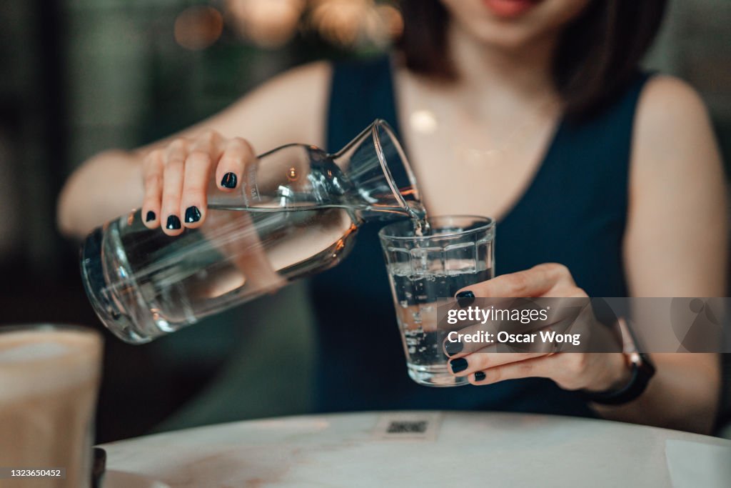 Cropped Shot Of Young Woman Pouring Water To A Drinking Glass At Cafe