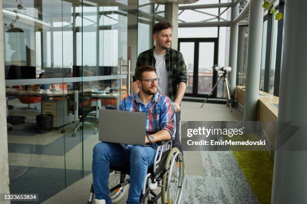 un homme d’affaires aide son collègue masculin en fauteuil roulant dans le hall d’entrée - accessibilité aux personnes handicapées photos et images de collection