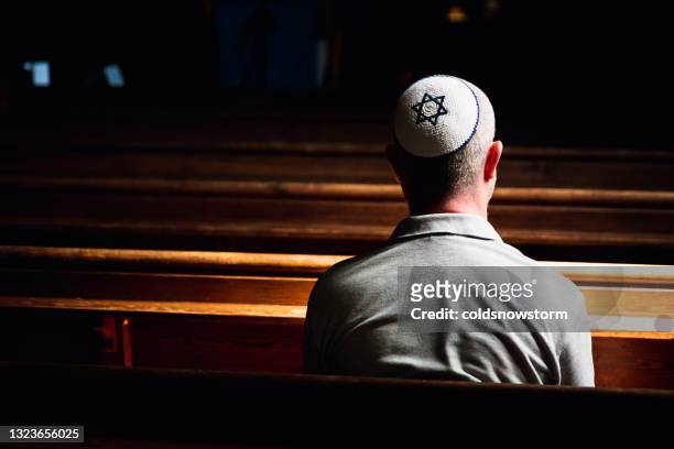 young jewish man wearing skull cap praying inside synagogue - jewish people stockfoto's en -beelden