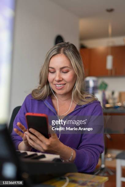 beautiful piano teacher teaches her virtual class while checking her cell phone to talk to her students - wfh celebrities stock pictures, royalty-free photos & images