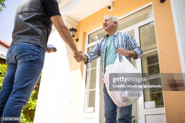 senior man greeting delivery man in front of house - eastern european man in front of house stock pictures, royalty-free photos & images