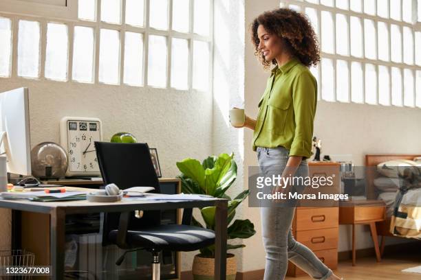 businesswoman with coffee cup walking toward desk - greenside stock-fotos und bilder