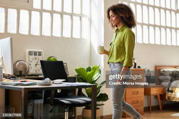 businesswoman with coffee cup walking toward desk - smart casual walking stock pictures, royalty-free photos & images