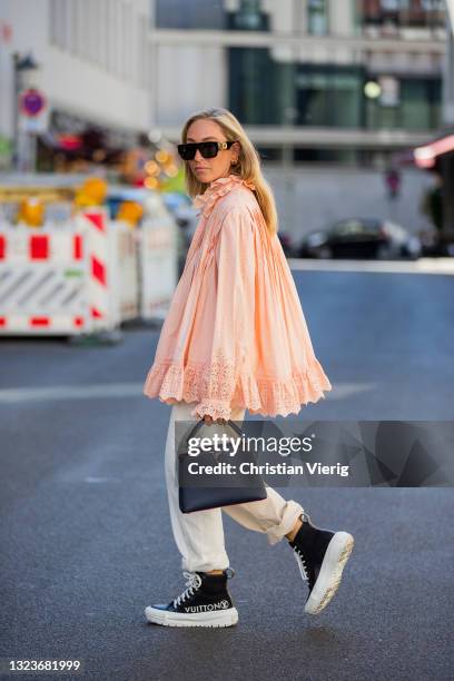 Sonia Lyson is seen wearing total look Louis Vuitton, salmon colored ruffled blouse, black bag, ankle sneakers with logo print, creme white pants,...