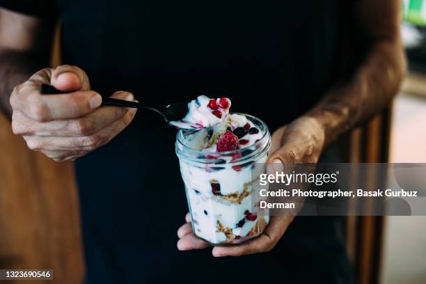 a man holding a jar of dessert made with yoghurt and frozen berry crunch - joghurt stock-fotos und bilder