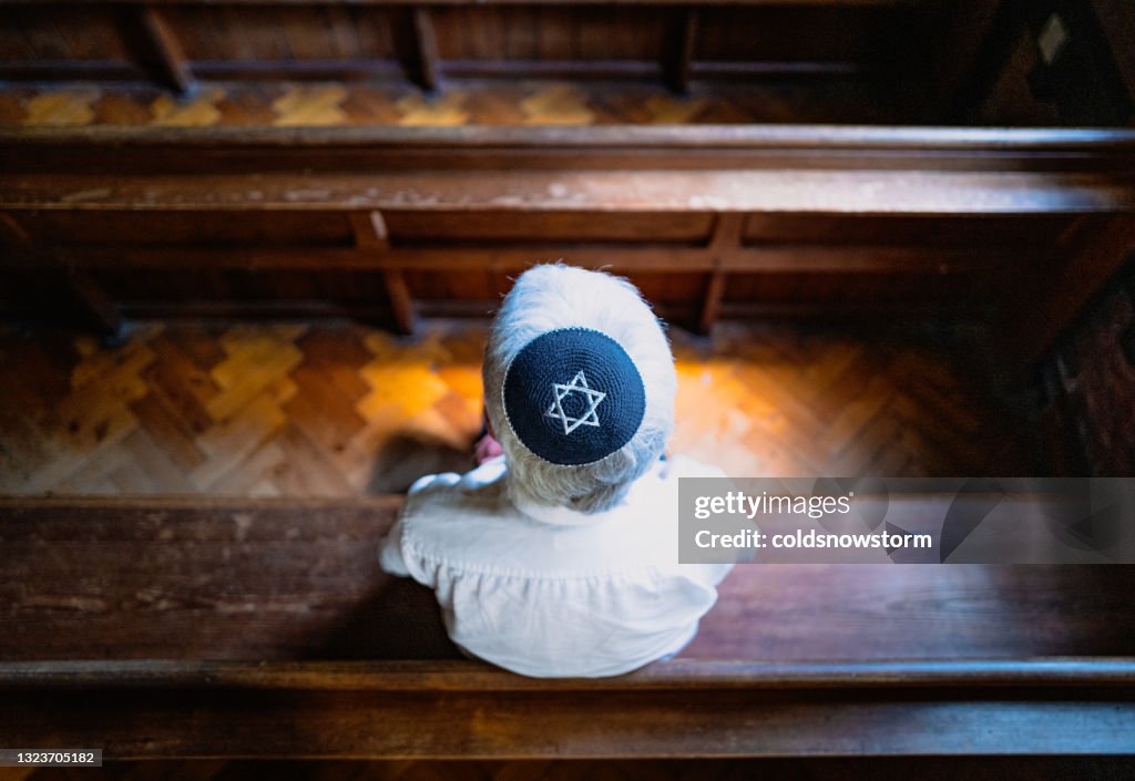 Senior Jewish man wearing skull cap praying inside synagogue