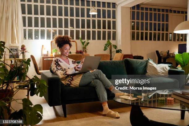 woman using laptop on sofa in living room - black interior stockfoto's en -beelden